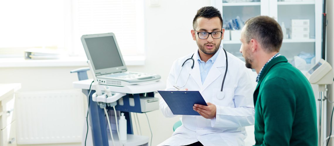Middle-aged bearded patient having consultation with highly professional physician at modern office, they discussing diagnosis and possible treatment