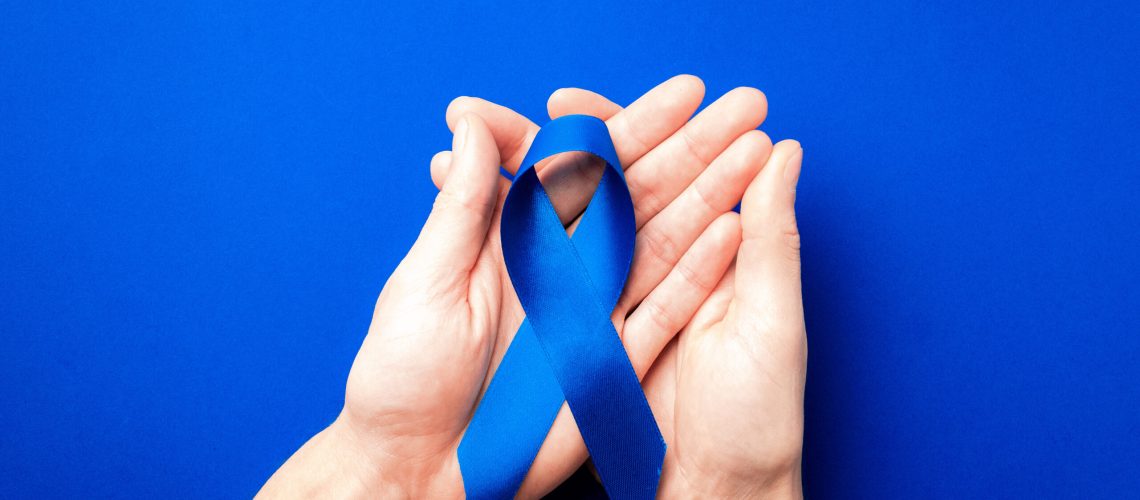 Blue prostate ribbon. Awareness prostate cancer of men health in November. Blue ribbon in hands isolated on deep blue background. November and International Mens Day